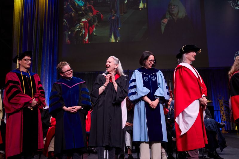5 Faculty members stand on stage at convocation in different gowns and hoods 