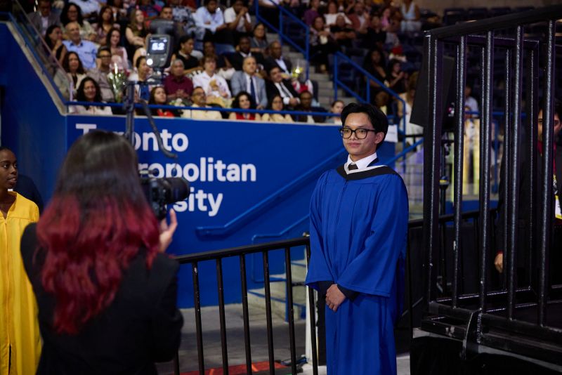 A grad in a blue gown is being photographed by a GradImages photographer at the bottom of the exit ramp. 