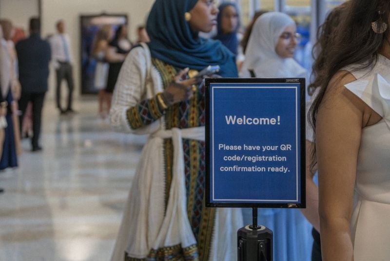 Graduands lined up in front of sign that says "Welcome! Please have your QR code/registration confirmatio ready"