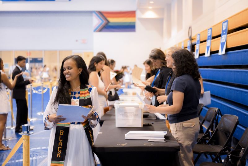 A grad in a white dress is picking up their award document from the Curriculum Advising table in the Varsity Court