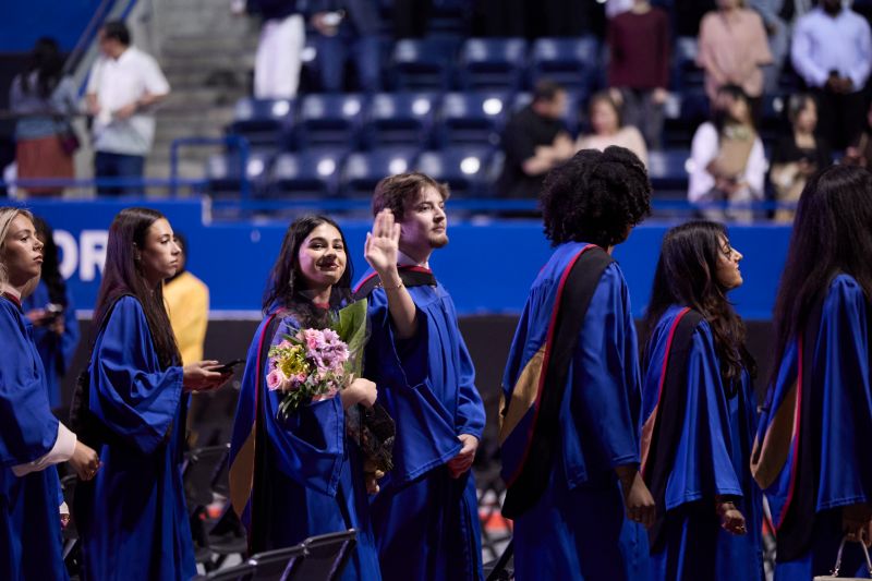 An overhead shot showing grads in blue gowns being led out of the arena and up to the 4th floor in two single file lines. 