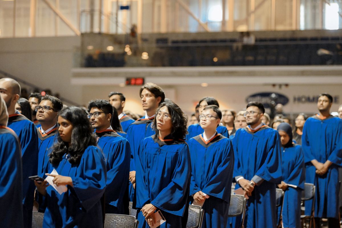 Graduands in blue bachelors gowns standing in the convocation arena
