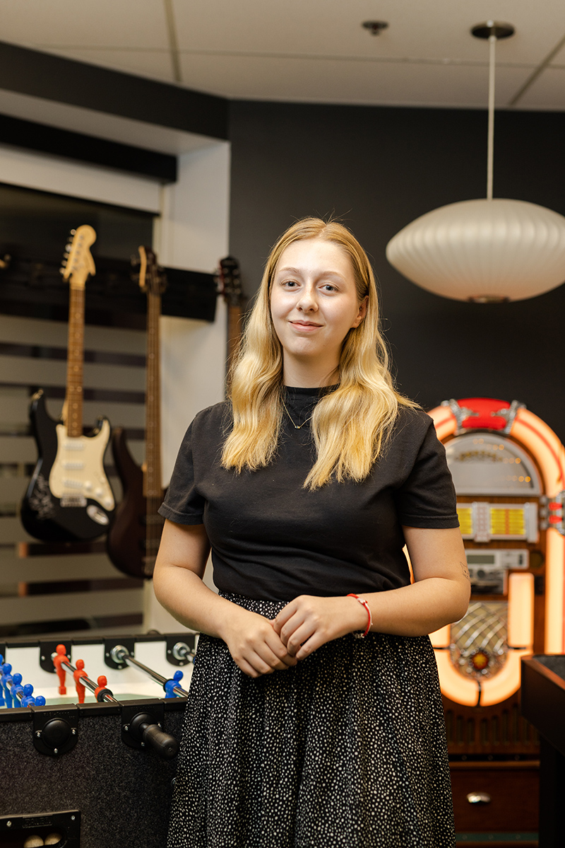 A person standing in a creative studio space with guitars and a vintage jukebox in the background.