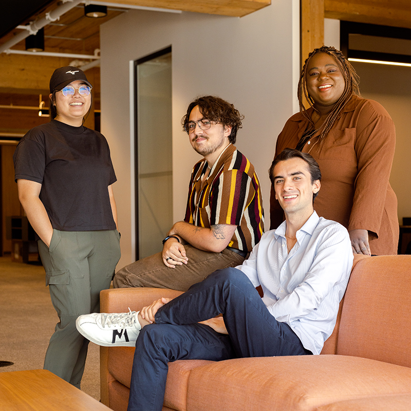 A group of four people posing together in a contemporary office lounge with wood beams and modern furniture.