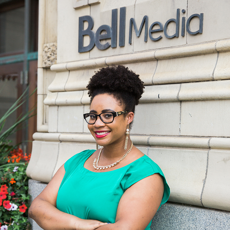 A person standing outdoors in front of a Bell Media building, smiling with arms crossed.