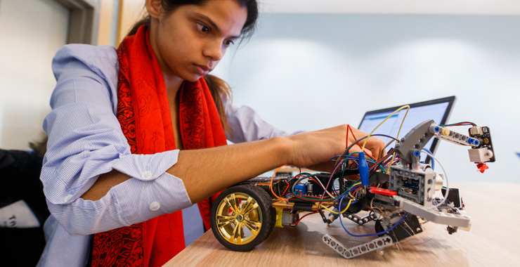 Computer science student working on robotic vehicle in class lab.