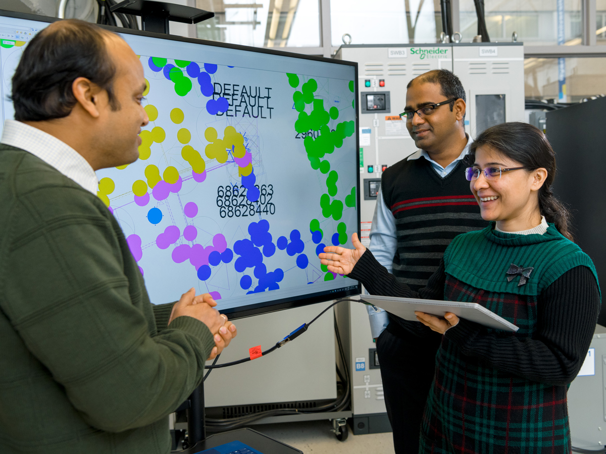 Two males and one female researcher standing by a screen.