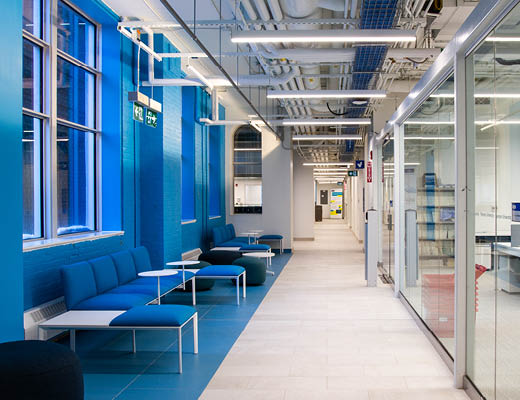 View of a hallway with blue walls and couches on the left side and glass paneling on the right side.