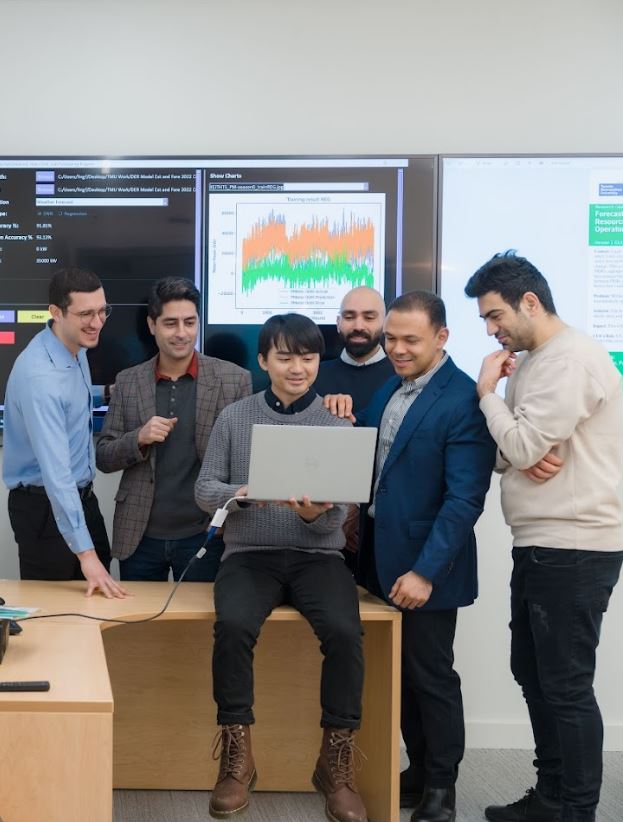 group of researchers looking at project on laptop together surrounding 1 holding the laptop