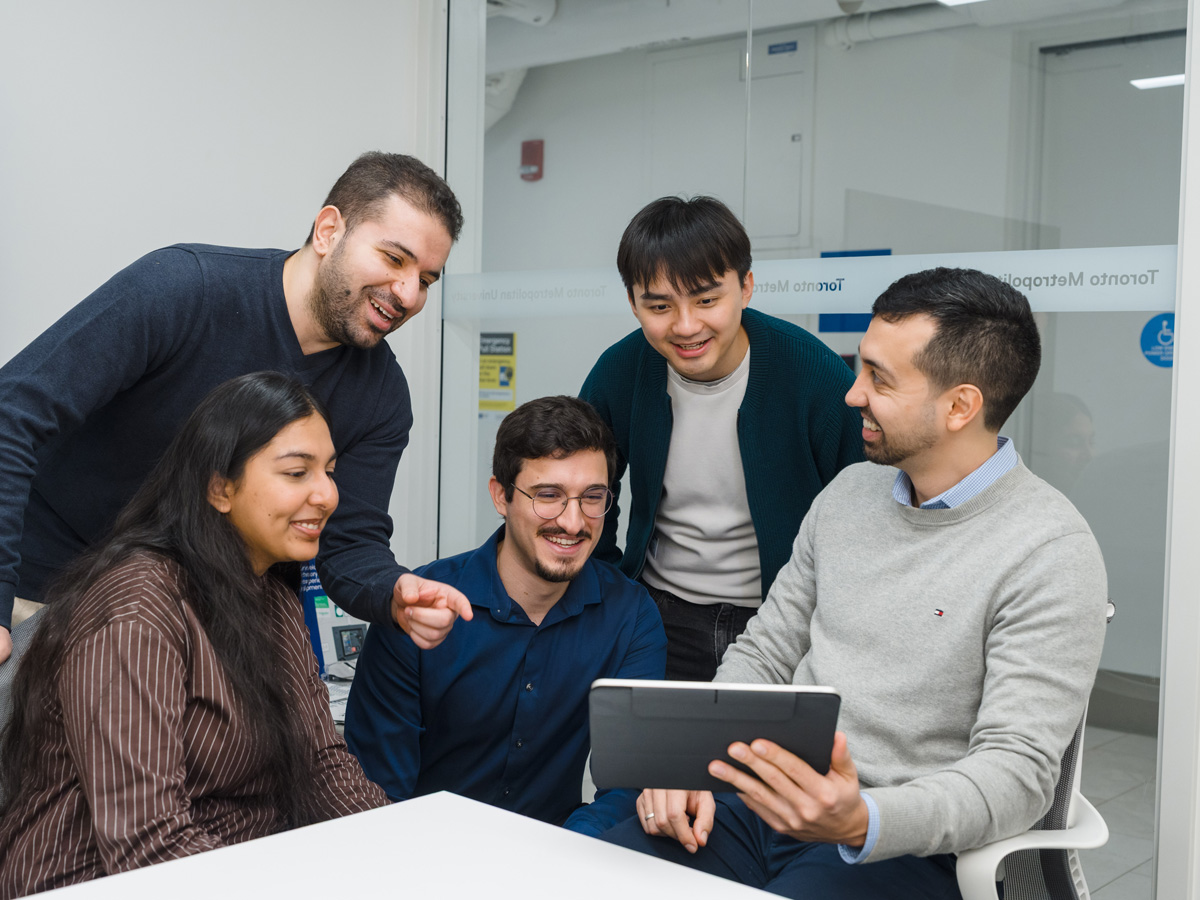 group of researchers looking at project on laptop together surrounding 1 holding the laptop