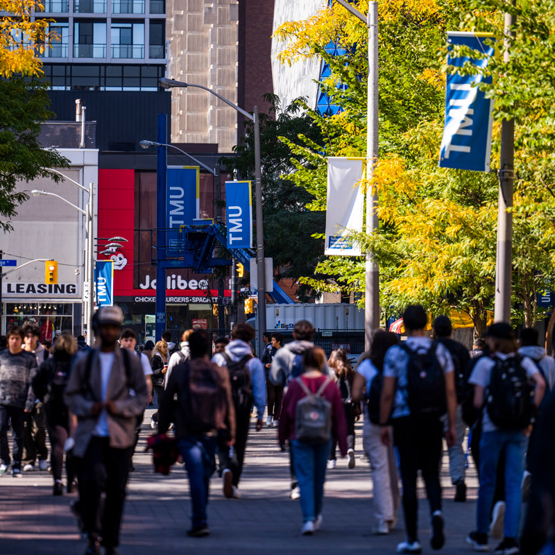 Students walk under the TMU banners on Gould Street on a sunny, autumn day.