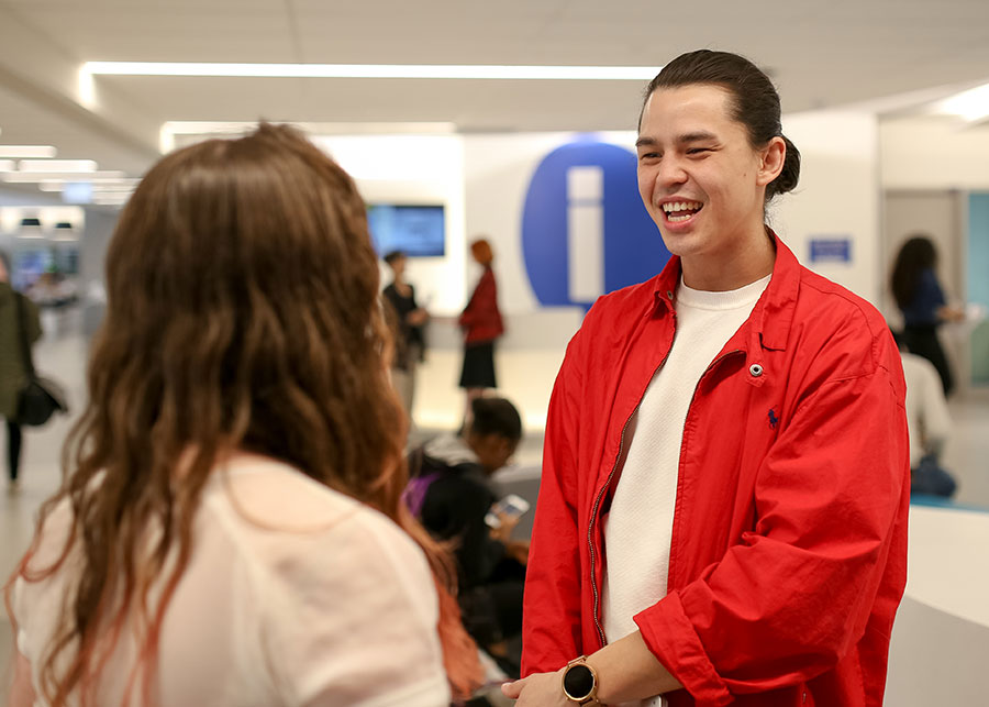 Two students talking to each other in the ServiceHub. One student has their back turned to the camera, while the other student is facing the camera and smiling.