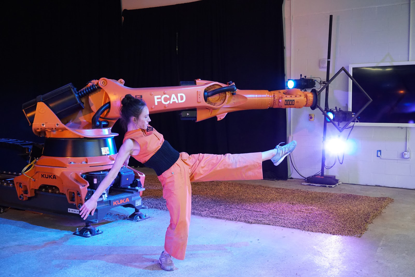 A performer poses dynamically in front of a robotic arm.