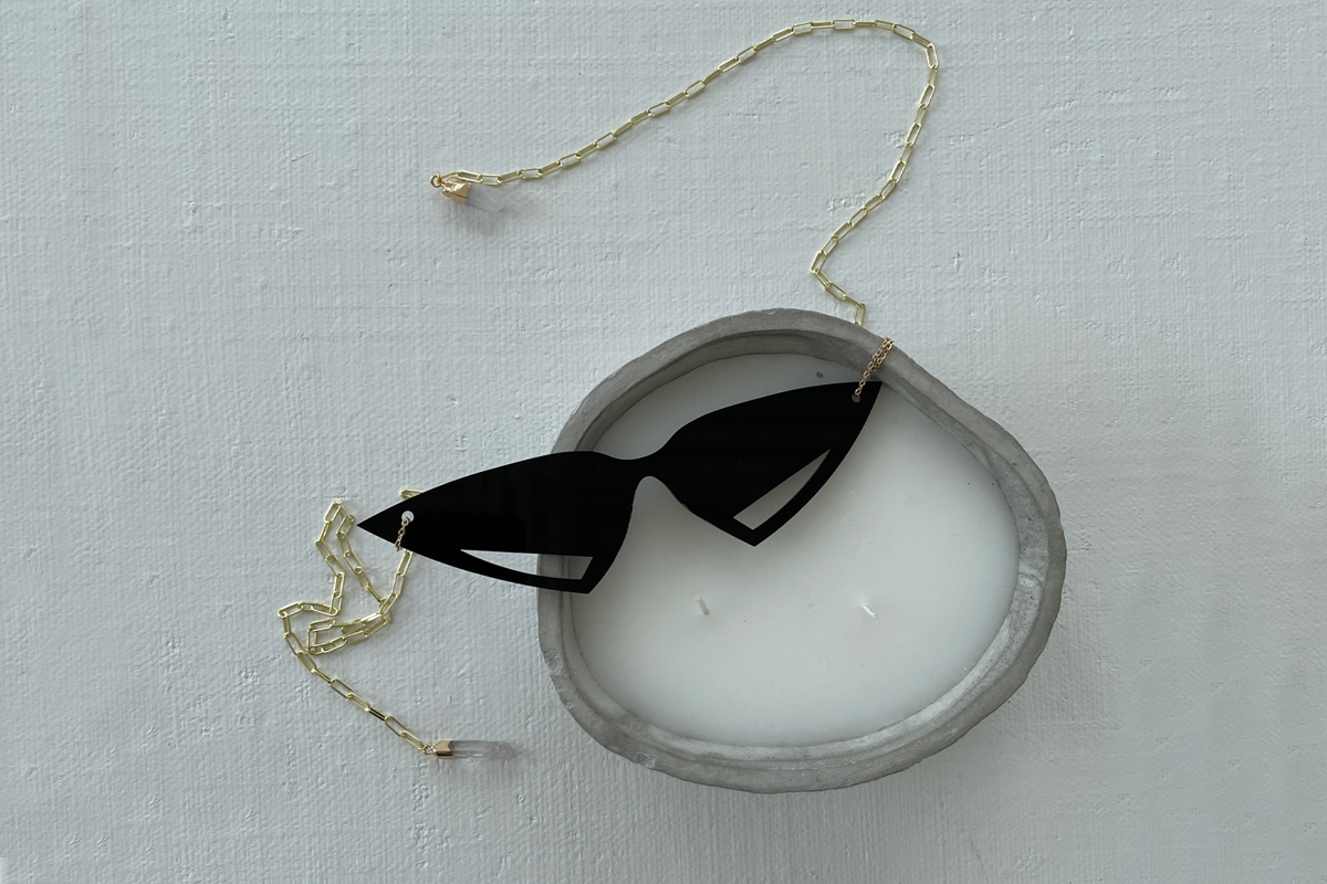 triangular sunglasses with gold chain attached from either side. The sunglasses are resting on a metallic ring.