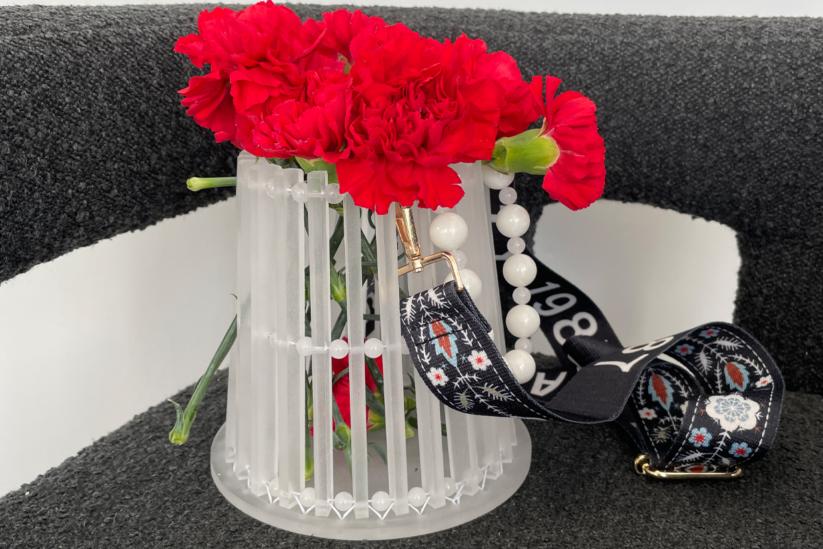 A cylindrical purse with pearl trim, holding a bundle of red flowers.