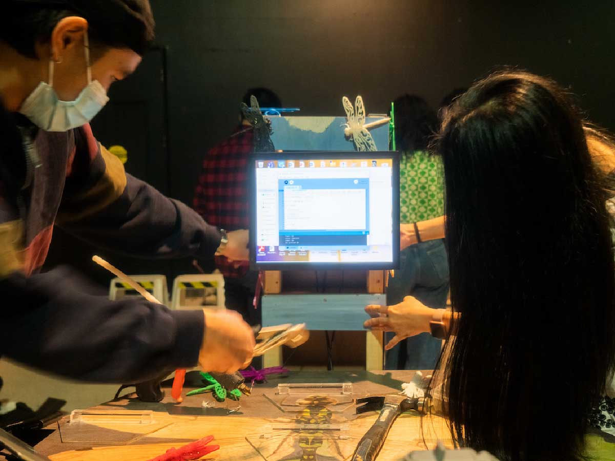 Students interact with a project. Someare looking at a screen, others hold wooden blocks.