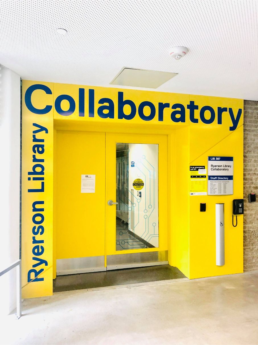 The Collaboratory entrance is a bright yellow doorway. There is an accessible door opener and phone to the right of the door.