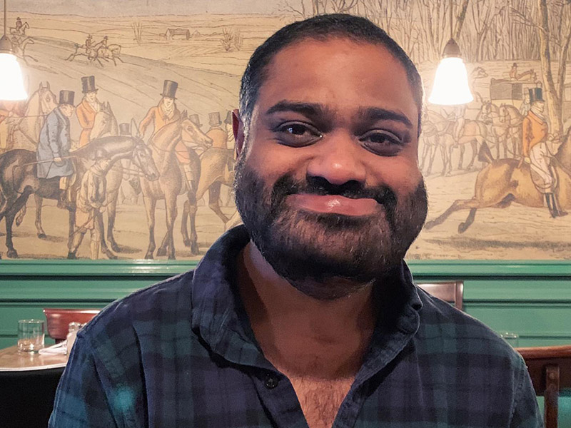 Ricky Varghese smiling, wearing blue checkered shirt