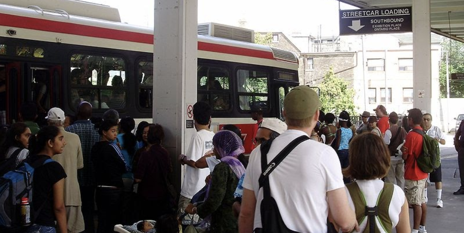 Image of people crowded around TTC bus waiting to board. 