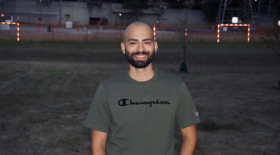 Vahid is wearing a green t-shirt and is standing outdoors in the evening/night on a grassy field.