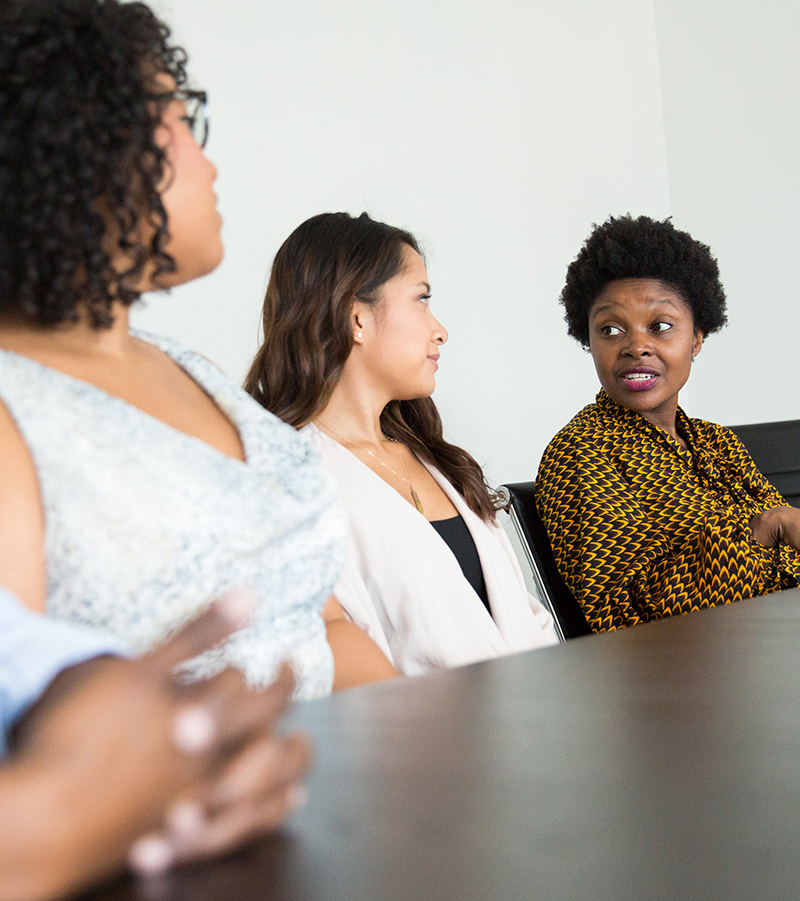 Three students of diverse racialized identities, including Black students, are sitting at a table having a conversation.