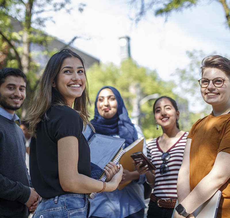 A group of five diverse students, standing outside on Gould street, smiling and looking towards the camera. 