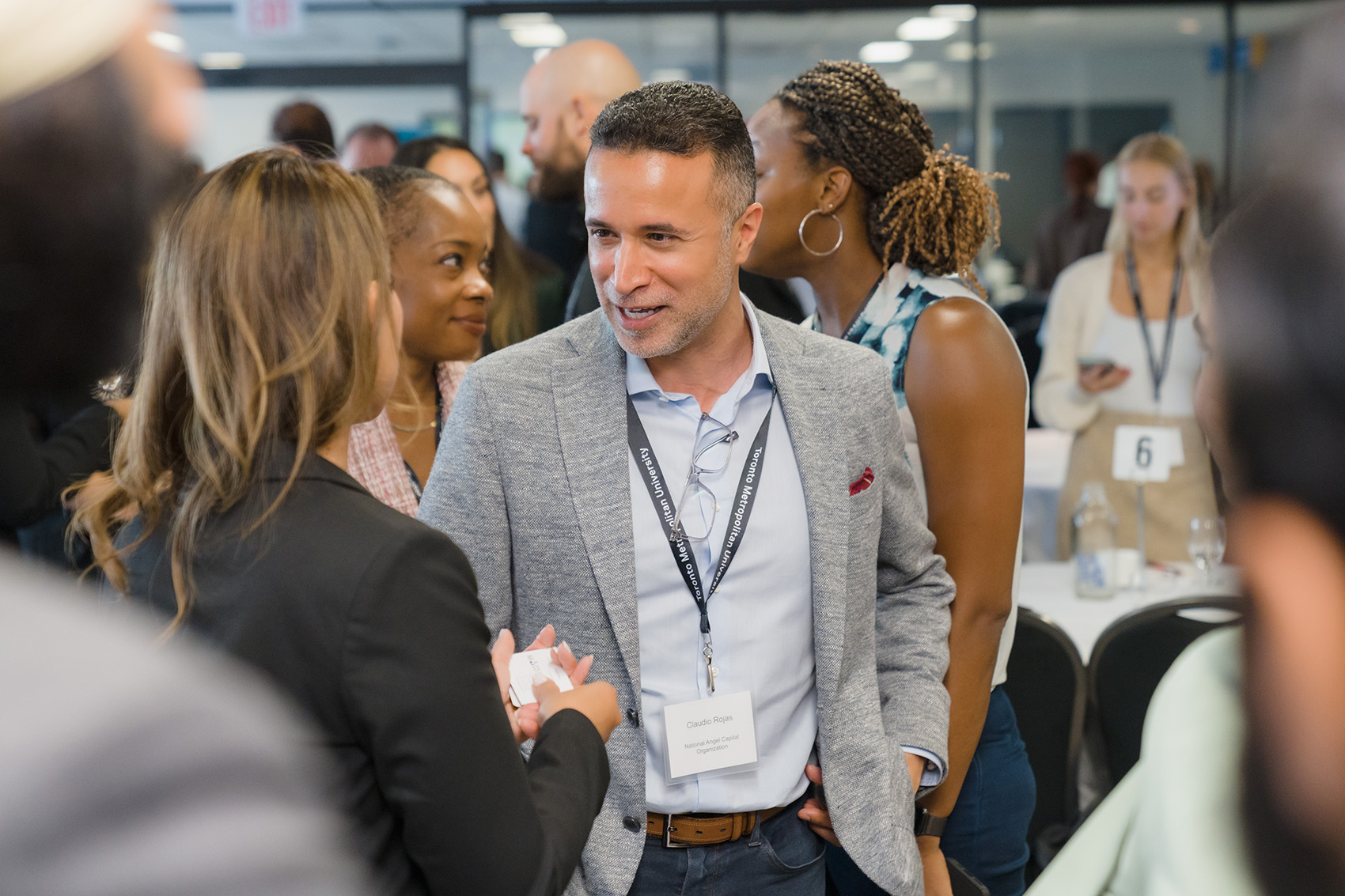 In a busy room, two folks in business casual attire converse.
