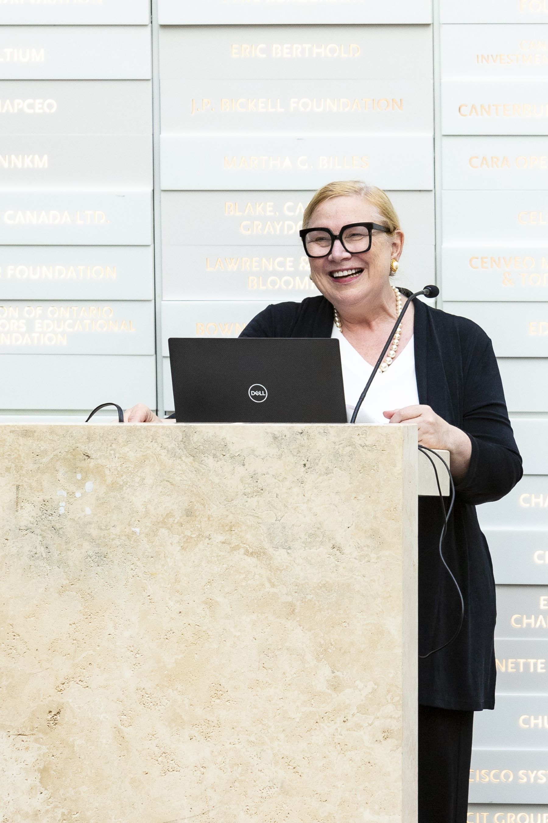 A professional woman smiles while she gives a speech at a podium.