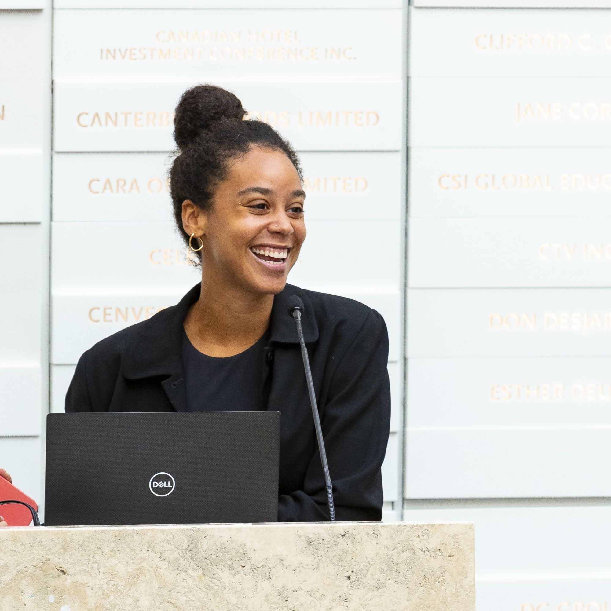 A young woman in business attire is smiling while speaking at a podium.