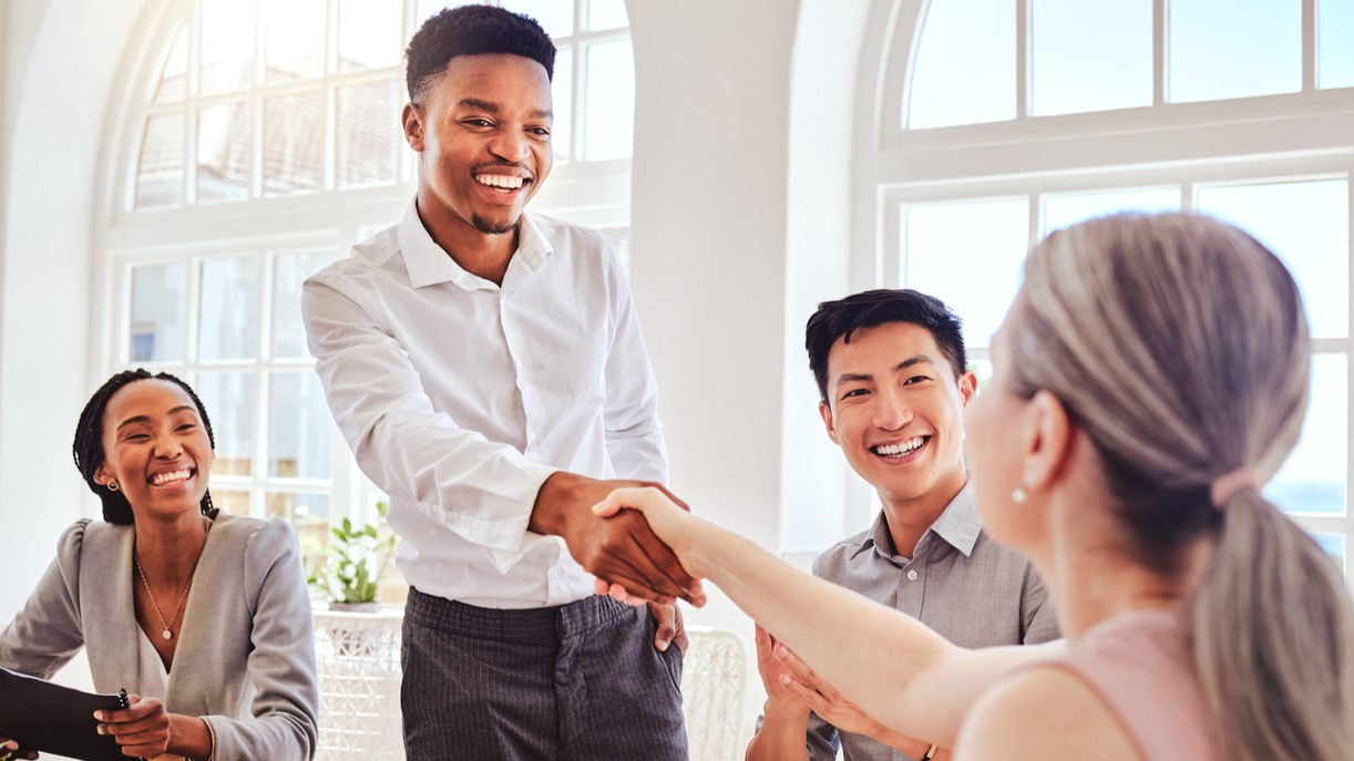 In an office setting, two young diverse people shake hands to solidify an employment opportunity. 