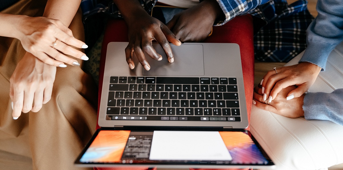 An image of a laptop computer with three people's hands gathered around it.