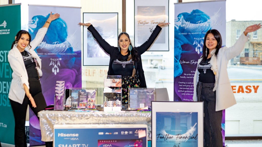 Three women smiling and standing at a booth with their products.