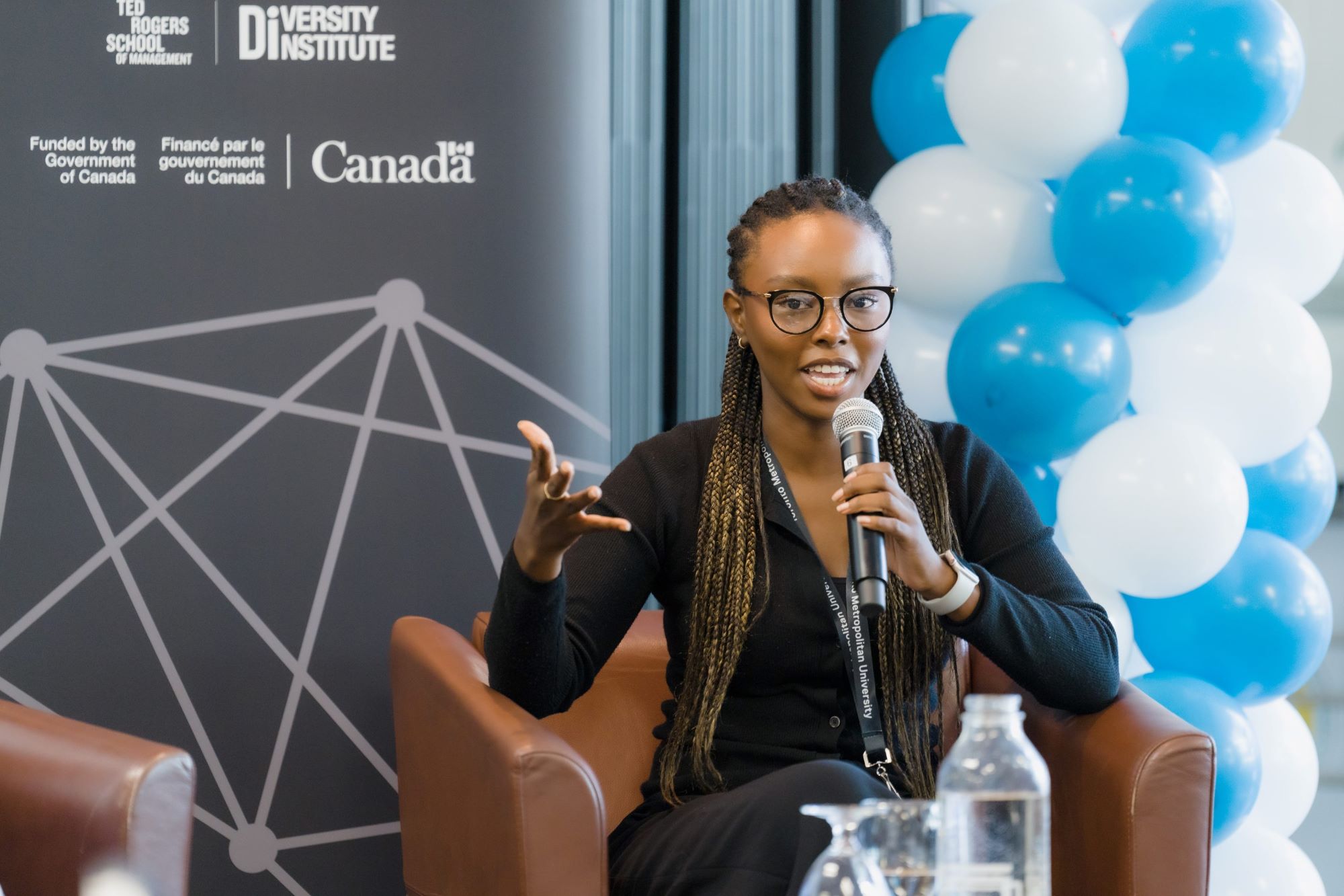 A young Black woman entrepreneur is seated during the panel conversation and speaks into a microphone.