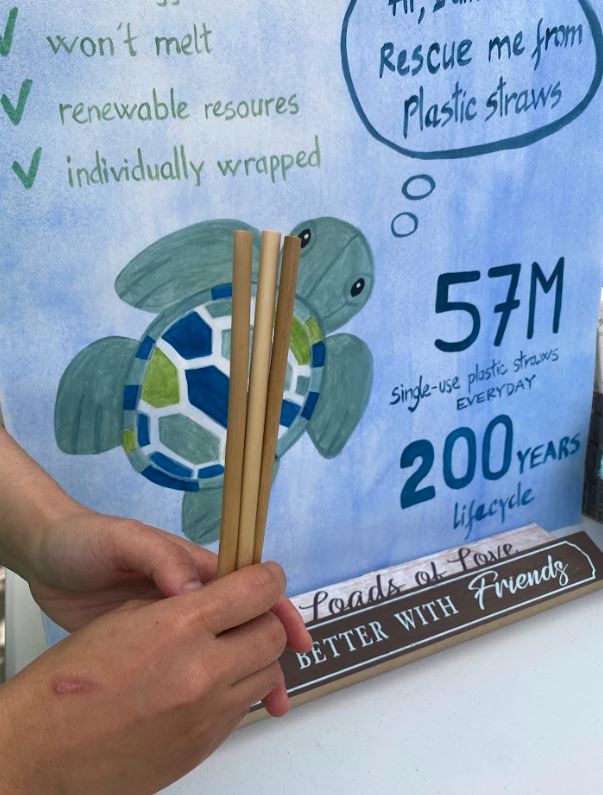At an outdoor market, bamboo straws are displayed in front of a handmade sign promoting sustainability.