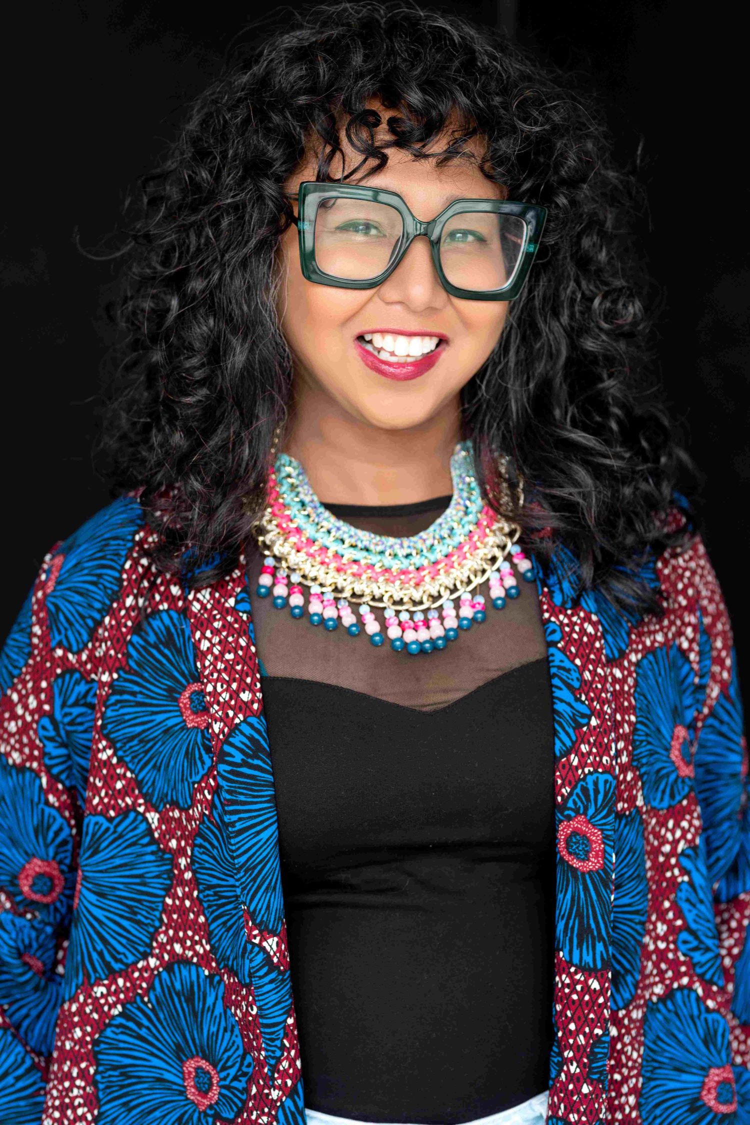 Veronica Antipolo has curly hair. She's wearing big glasses and smiling. 