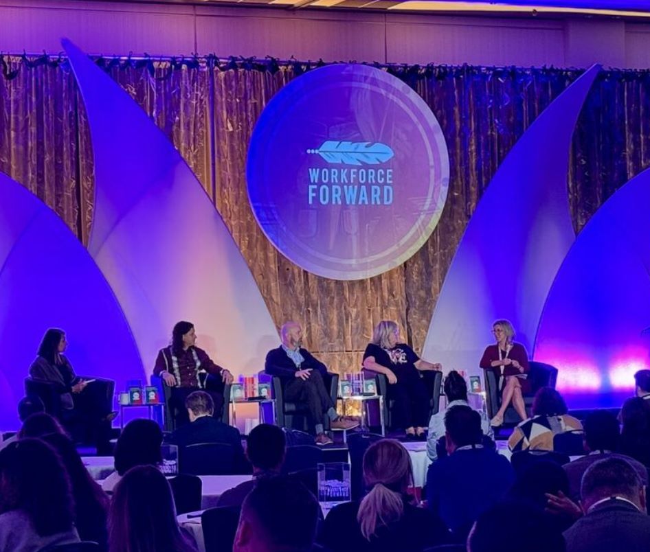 Five people are seated on stage, participating in a panel discussion. 