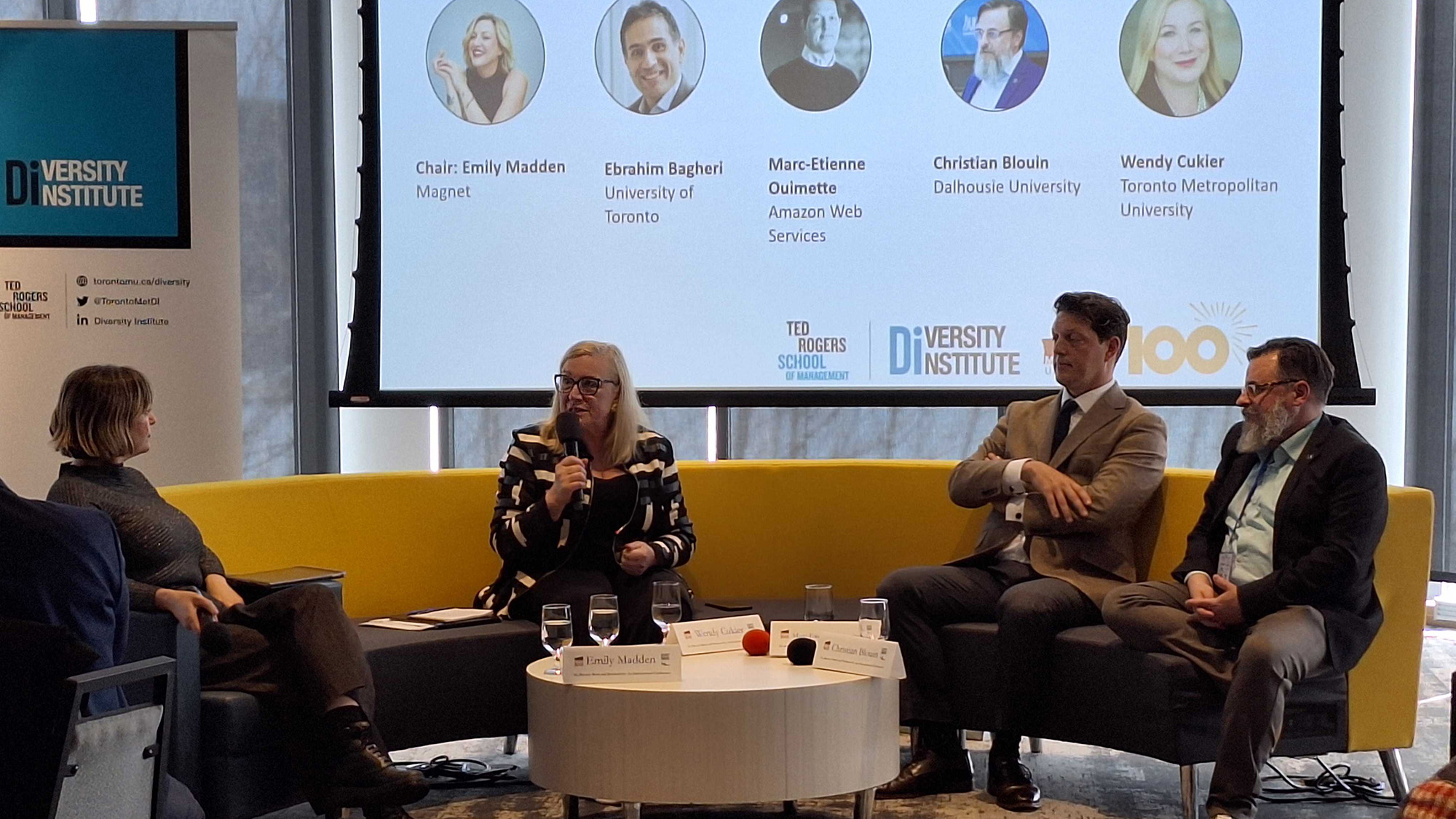 Four people sit on a couch in front of a projector for a panel discussion.