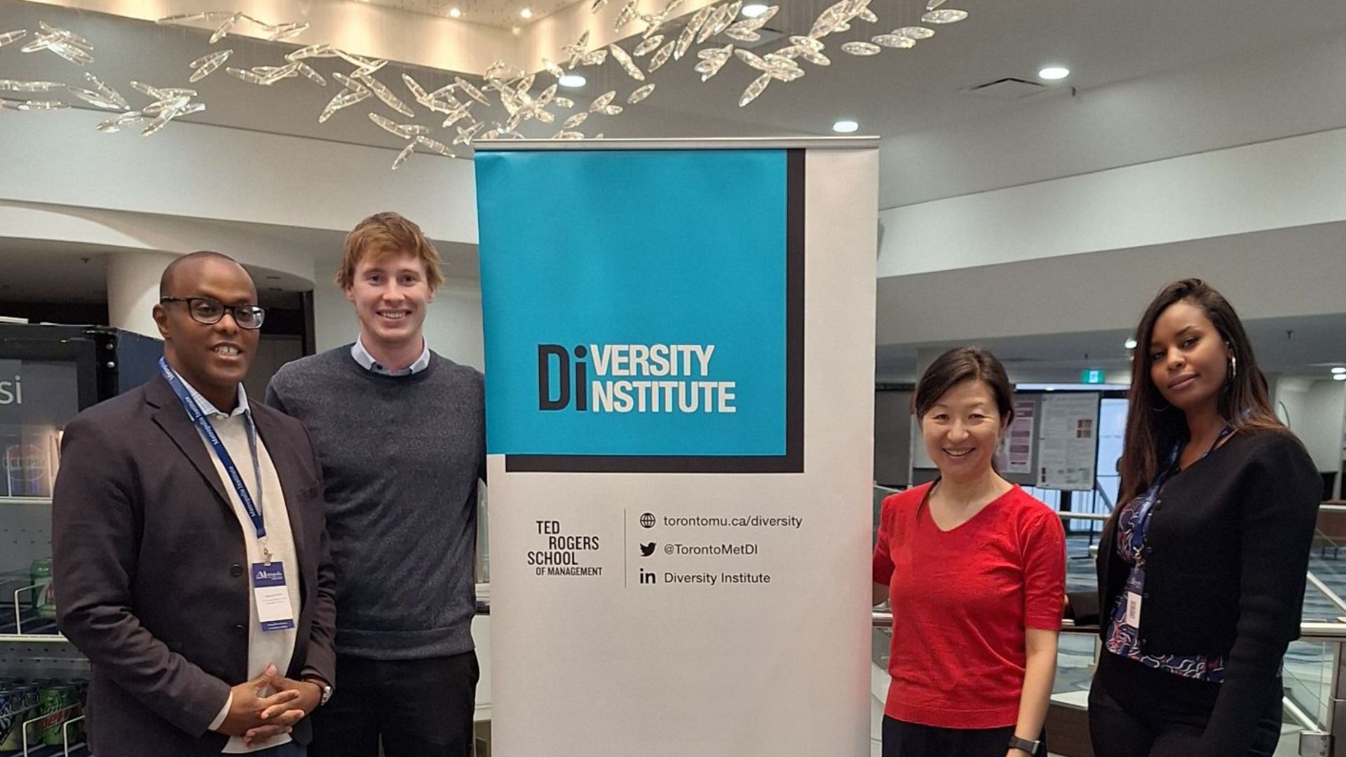 Four people in business casual attire pose for a photo with a banner. 