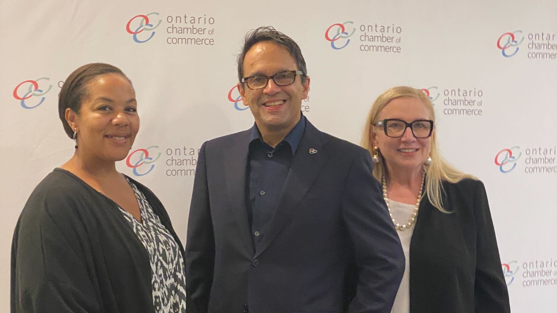 Three people at a business conference are smiling for a group photo. 