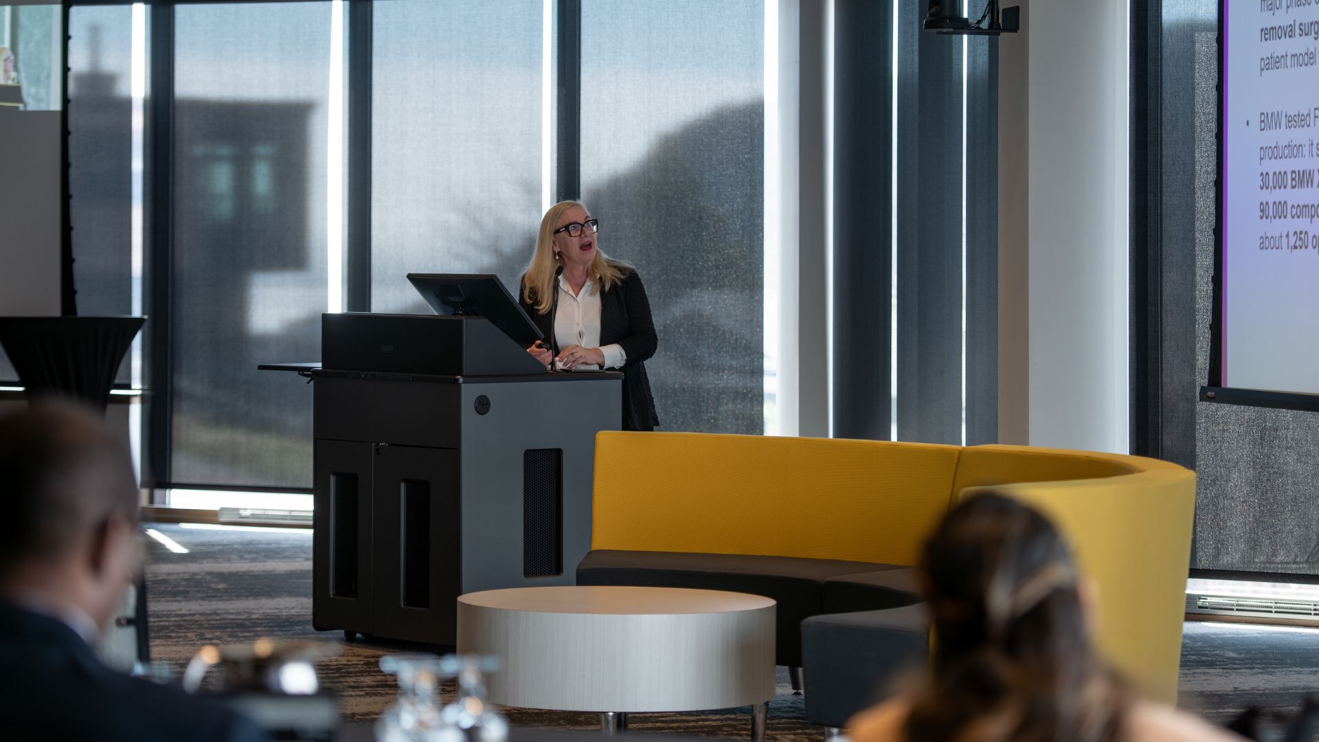 In a conference room, a woman conducts a presentation to a large crowd.