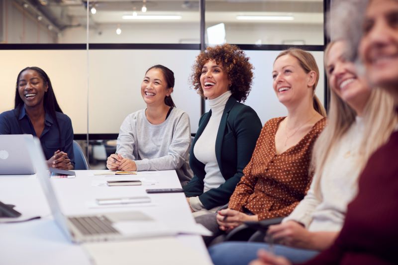 In an office setting, a group of diverse women work collaboratively.