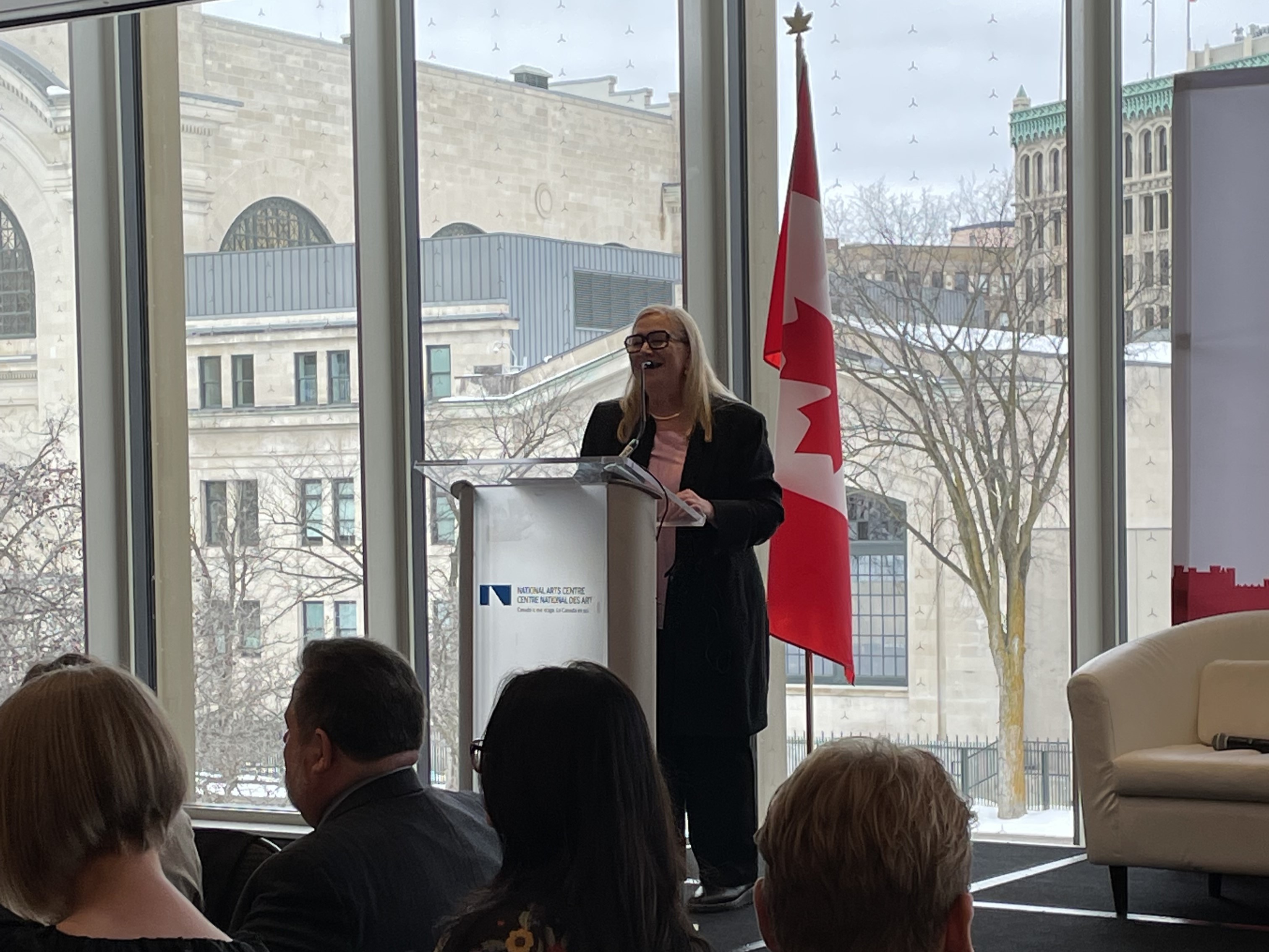 A woman standing at a podium speaking to an audience.