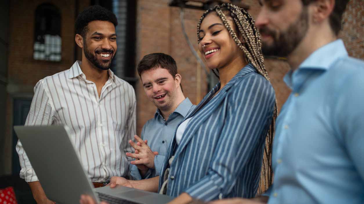 A group of young people working collaboratively in front of a laptop.