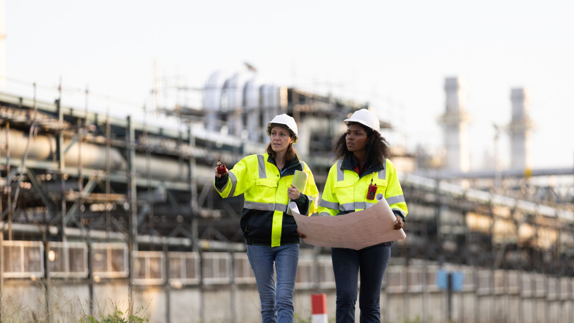 Two women walk through a large construction site.
