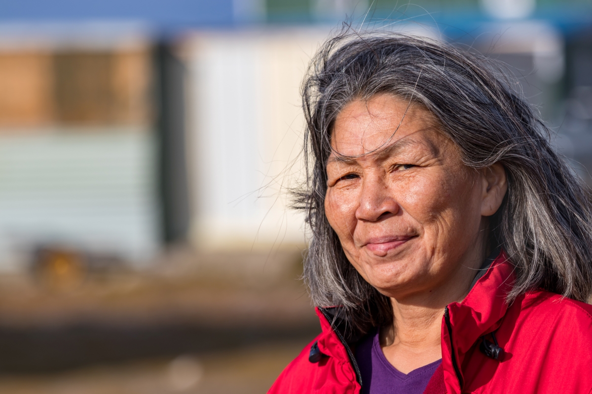 A mature woman in a red parka stands outside on a sunny day.