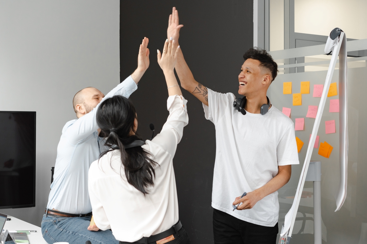 Three people, including one Indigenous man, high-fiving each other in a meeting room.