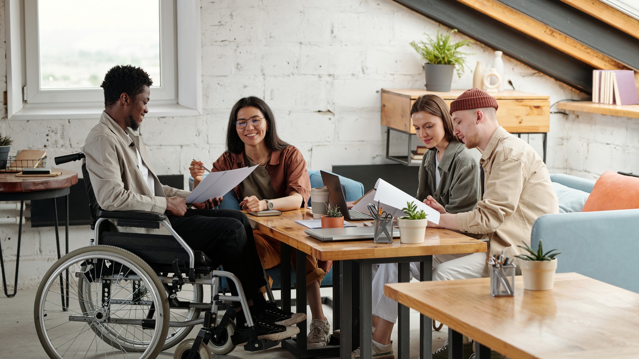 In a modern office, four people work together around a table. One person is in a wheelchair. 