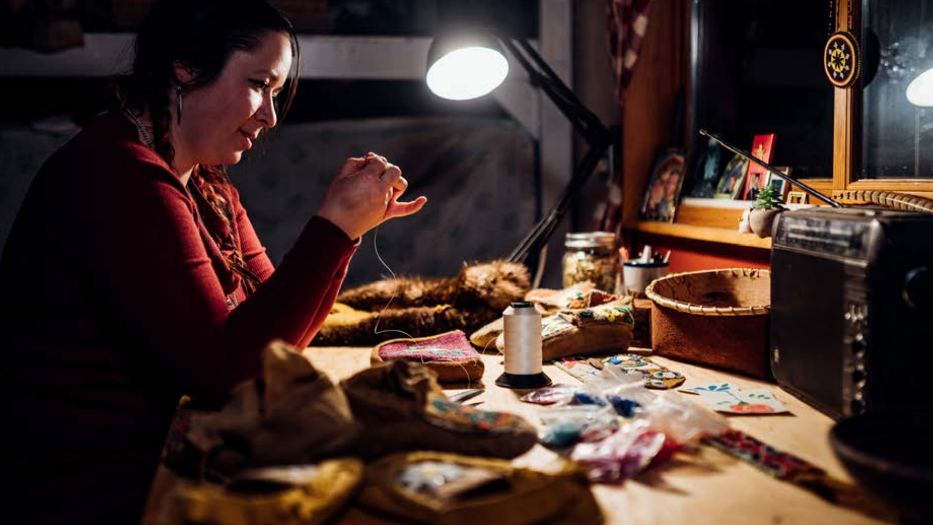 A woman works with beads under a bright lamp. 