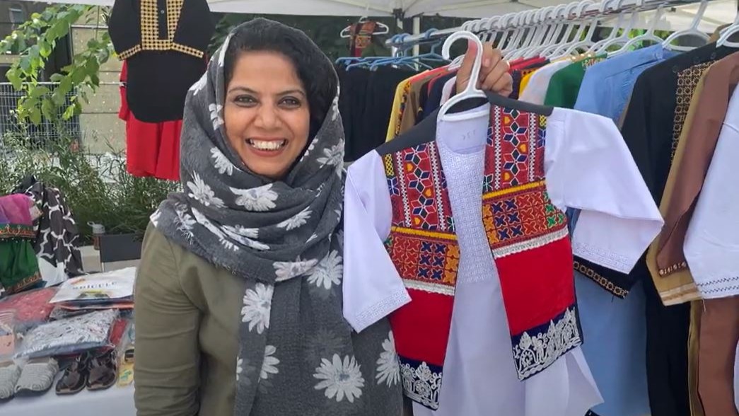 One woman smiles and is showing off a traditional Iranian boys outfit.