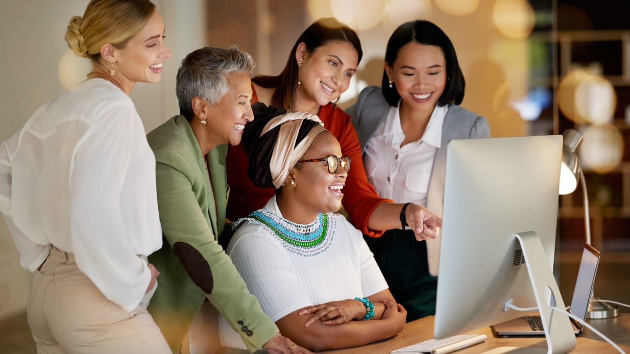A group of women work together at a computer.